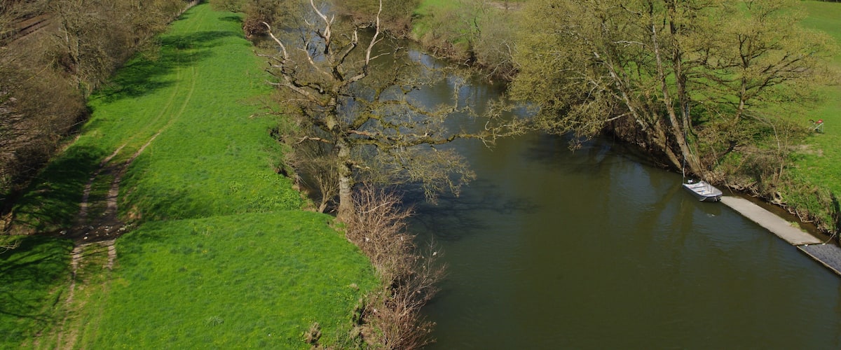 A river flowing through a green valley with trees and hills in the background.