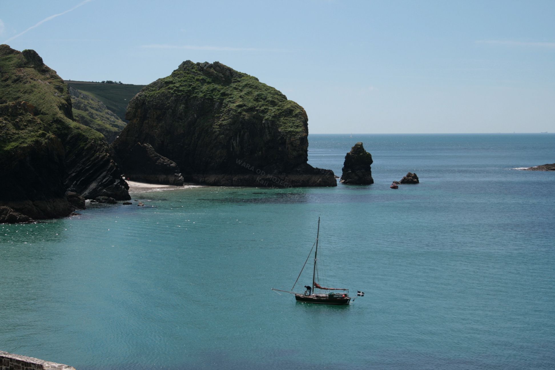 A sailboat on a calm sea with rocky cliffs and clear skies.