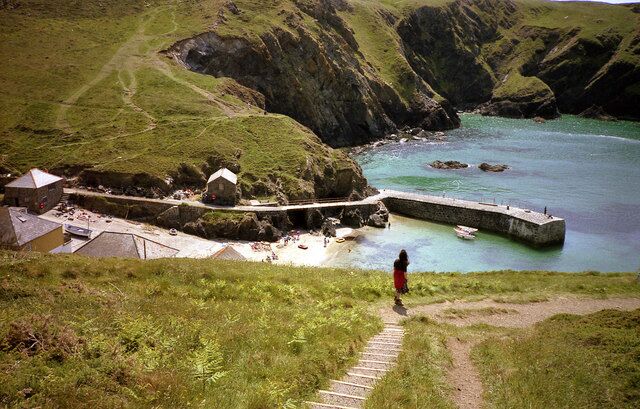 A coastal landscape with a stone pier, grassy hills, and a small settlement.