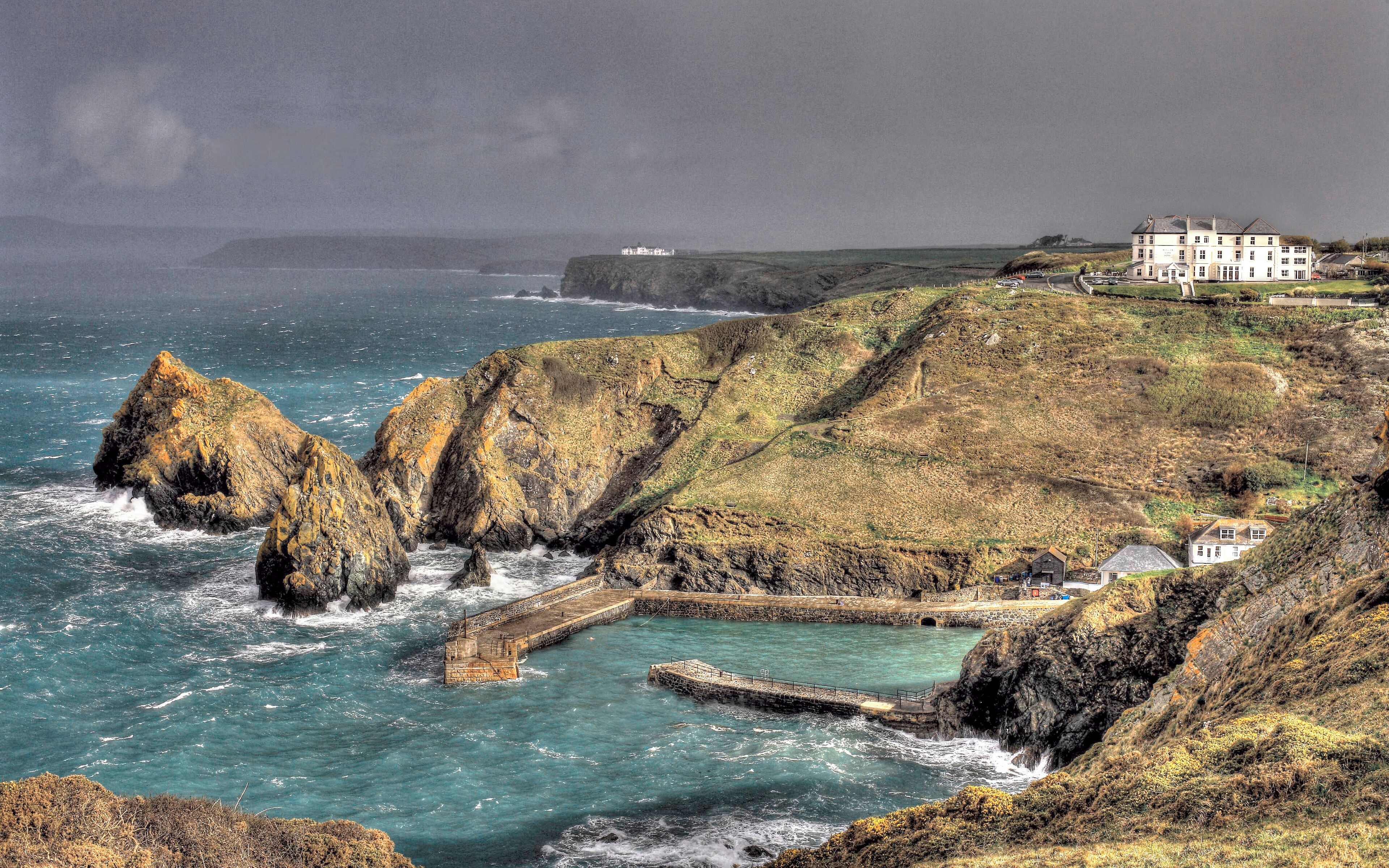 A coastal landscape with rocky cliffs, a lighthouse, and a large white building on a hill.