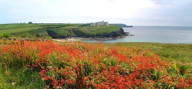 A coastal landscape with a grassy hill, a building on the hill, and a body of water.