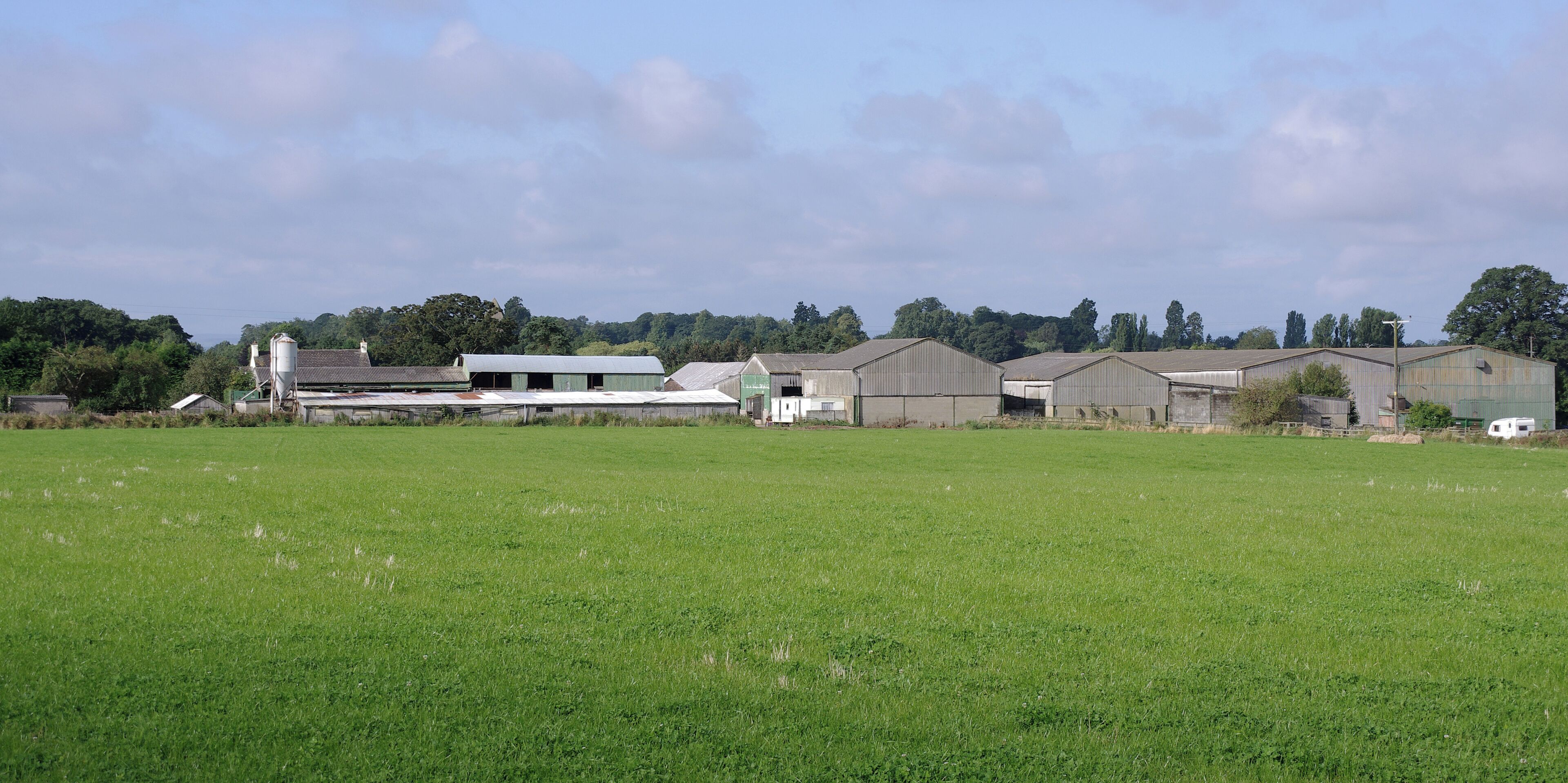A rural landscape with green fields, several farm buildings, and trees in the background.