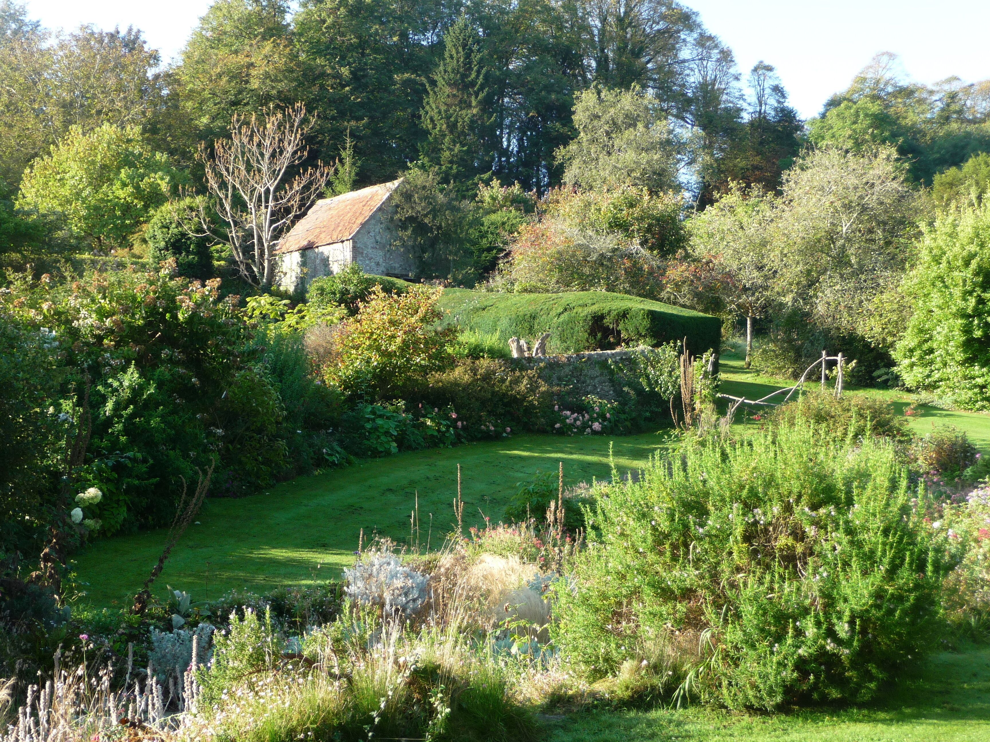 A lush garden with a stone house, a well-manicured lawn, and a variety of flowering plants.