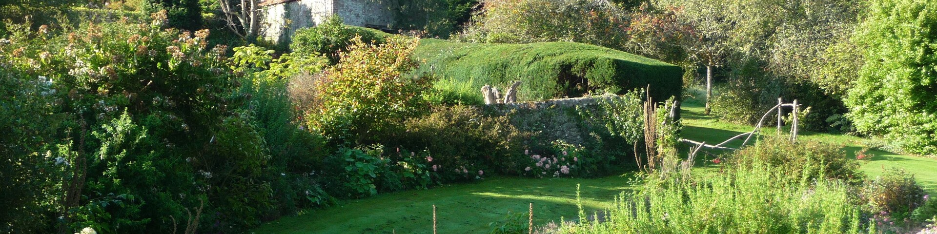 A lush garden with a stone house, a well-manicured lawn, and a variety of flowering plants.