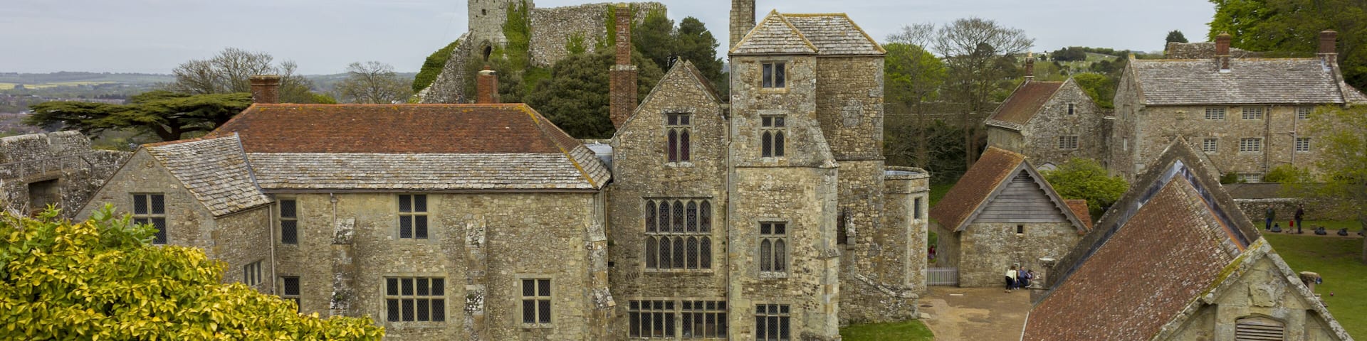 A historic stone building complex with a prominent tower, surrounded by lush greenery and a clear sky.