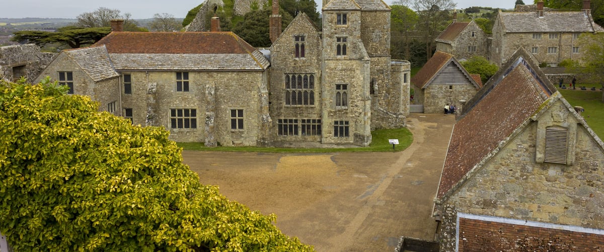 A historic stone building complex with a prominent tower, surrounded by lush greenery and a clear sky.