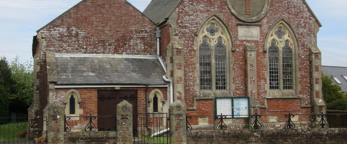 A historic brick church with a cross on the front, a bell tower, and a small annex building.