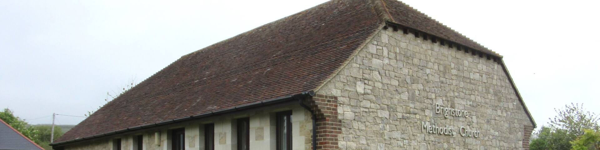 A stone Methodist Church with a brick base and a tiled roof.