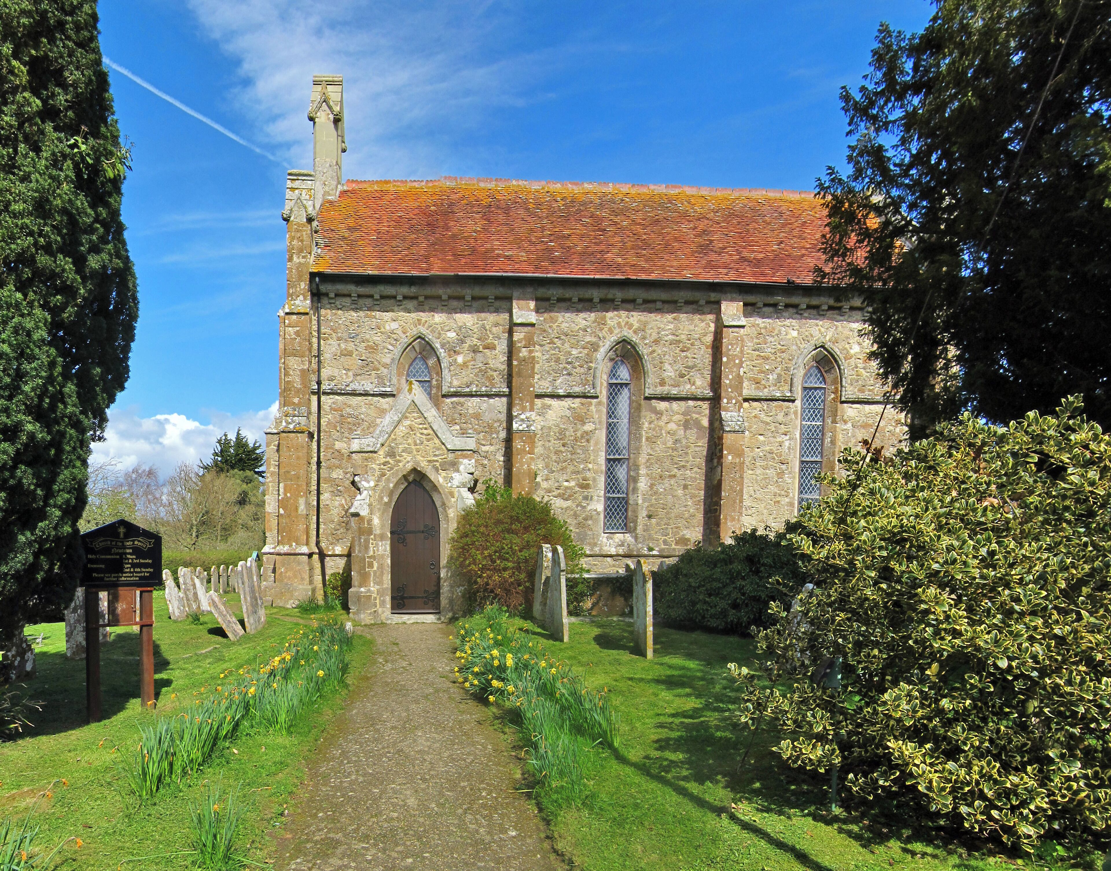 A stone church with a tiled roof, a central arched doorway, and a path leading to it.