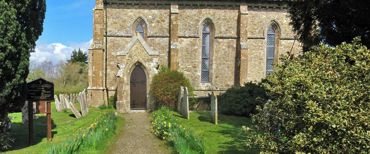 A stone church with a tiled roof, a central arched doorway, and a path leading to it.