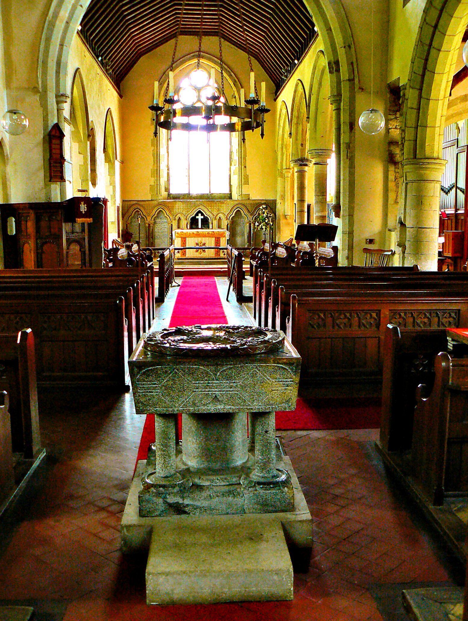 The font and the altar area of this old 11th century church. Located in Arreton village on the Isle of Wight. Originally built by the Normans.