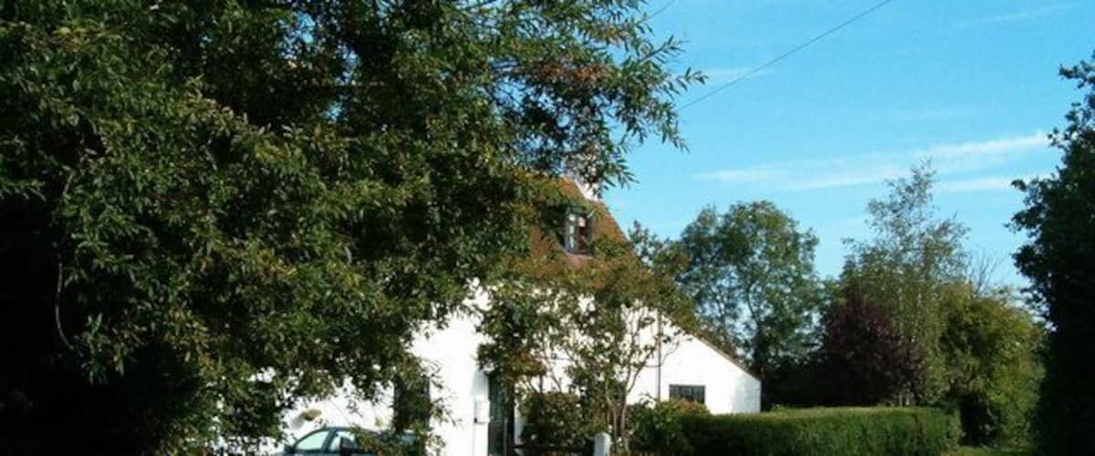 A rural road with a white house, a wooden fence, and a gate.