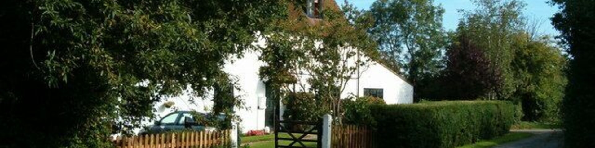 A rural road with a white house, a wooden fence, and a gate.