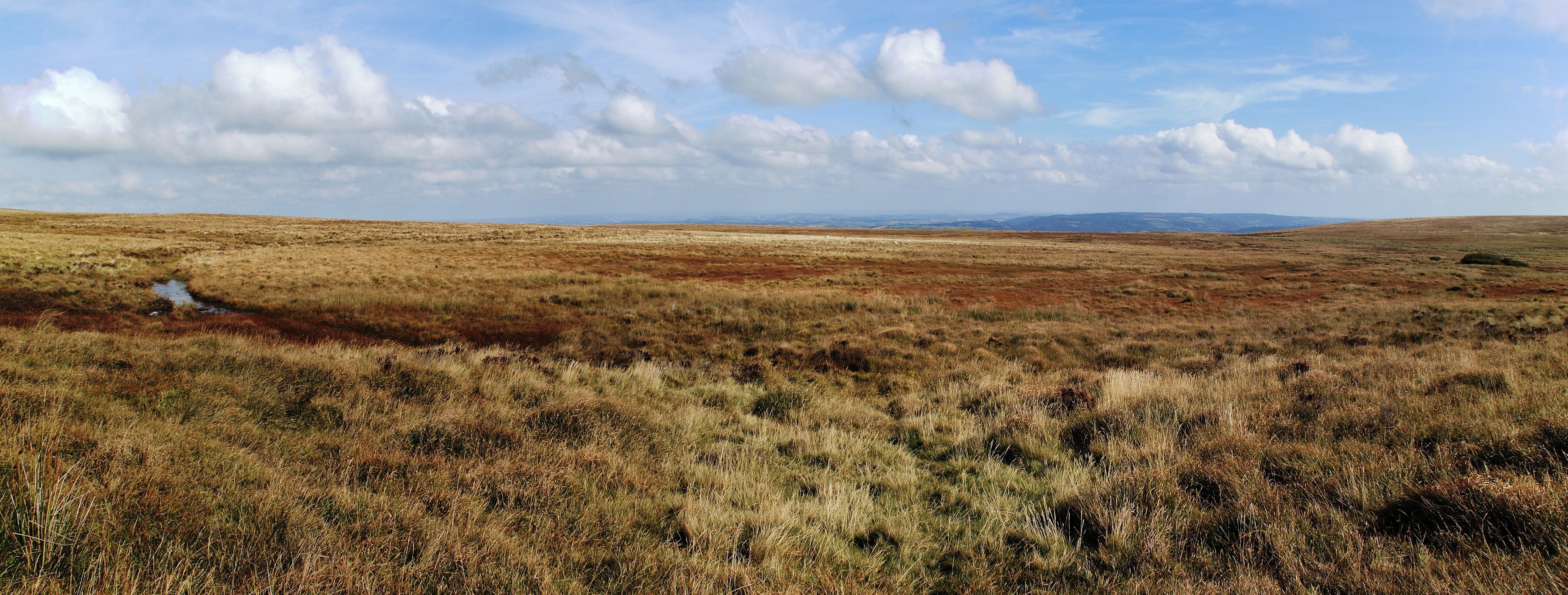 A vast, open landscape with rolling hills and a small stream.