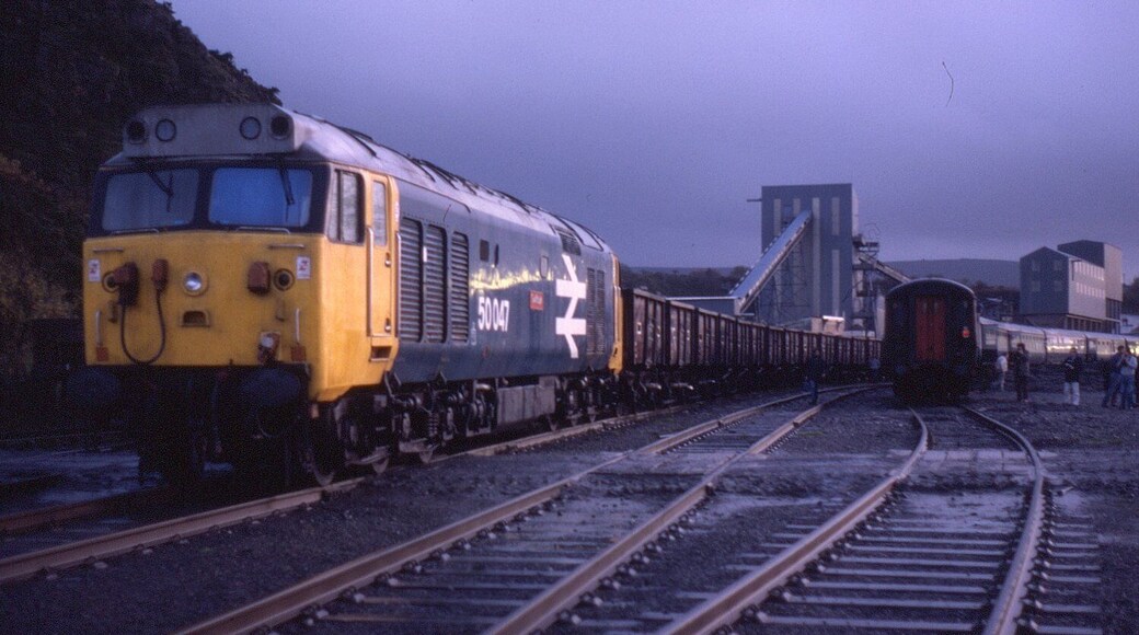 Taken during a photo stop on the Hertfordshire Railtour "Meldon Quarryman" on 24 November 1984. In falling light conditions at Meldon Quarry, 50047 "Swiftsure" is seen stabled on a train of stone wagons. Class 50s were never that common on freights being built originally for express services north of Preston on the WCML prior to electrification in mid-1970s. After that, they had a career move to be re-allocated to the Western Region and again worked express serves to the West Country. They also put in a good service during the 1980s on the London Waterloo to Exeter route.
