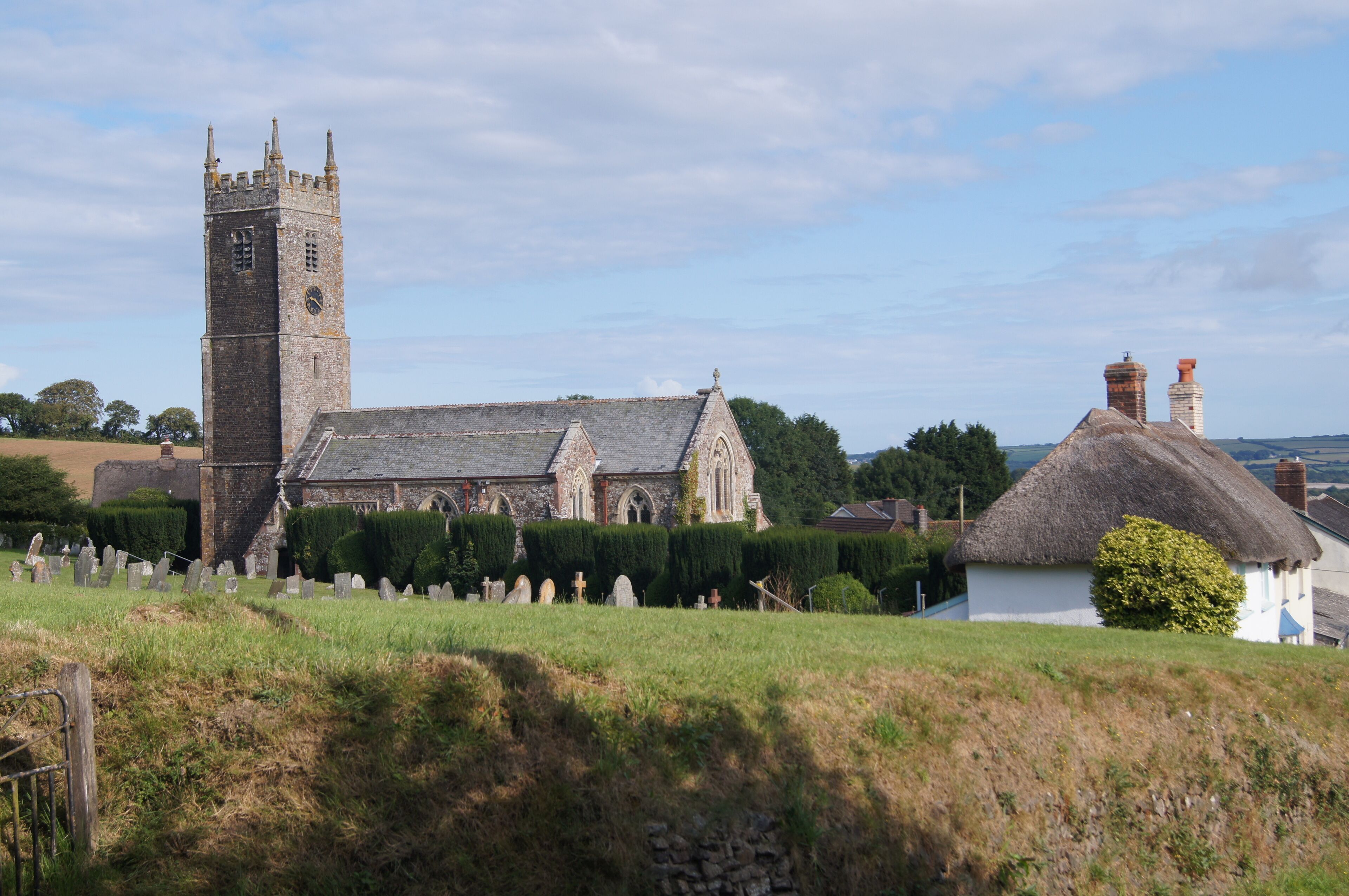A church with a tall tower and a thatched-roof house.