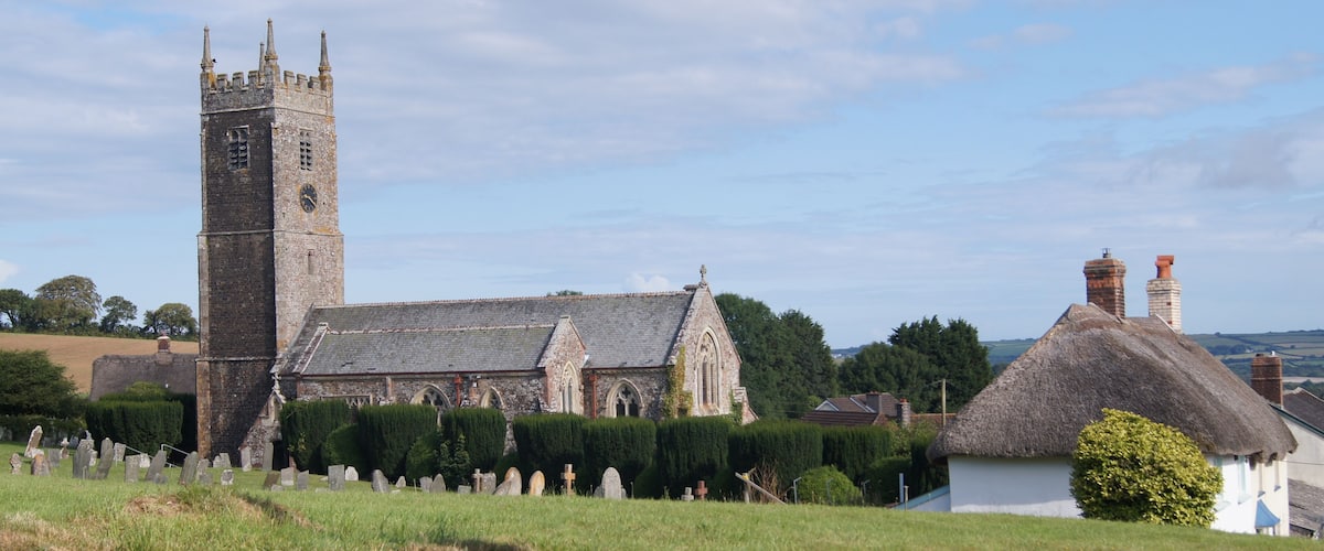 A church with a tall tower and a thatched-roof house.
