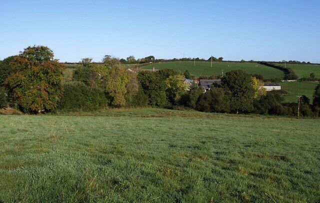 A rural landscape with rolling hills, a field, and scattered trees.