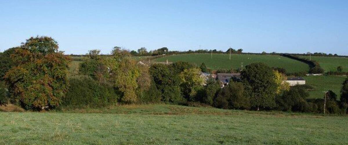 A rural landscape with rolling hills, a field, and scattered trees.