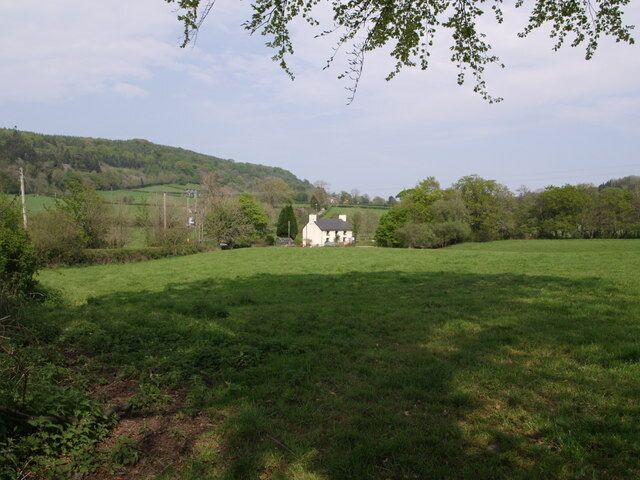 A rural landscape with a white house, green fields, and a hill in the background.