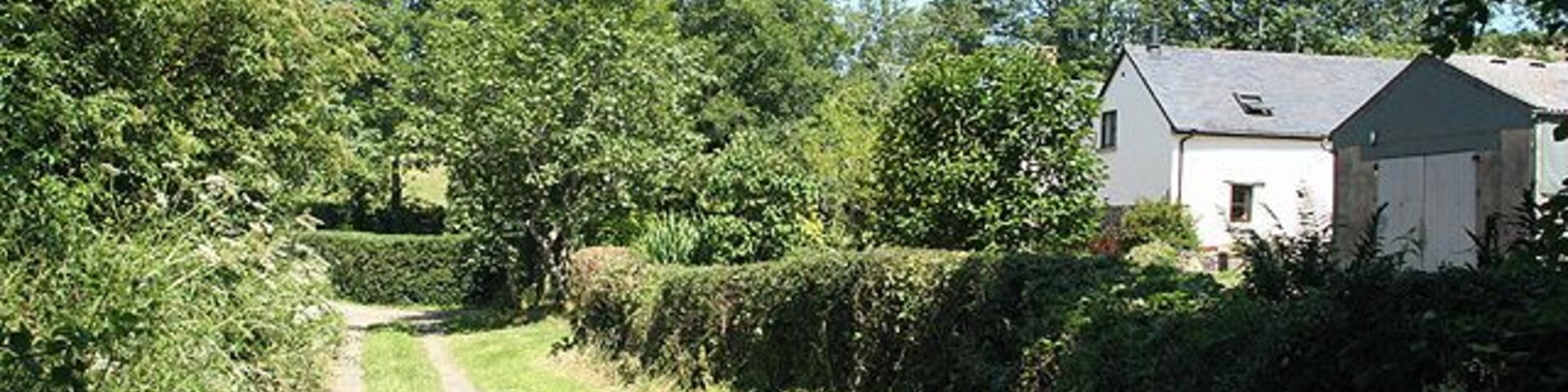 Un sendero rural que lleva a un edificio blanco rodeado de vegetación.