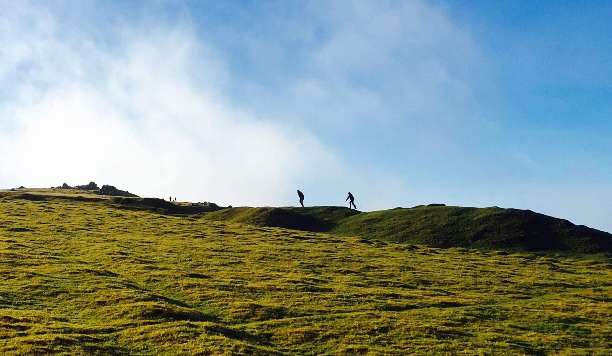A grassy hill with two people walking.