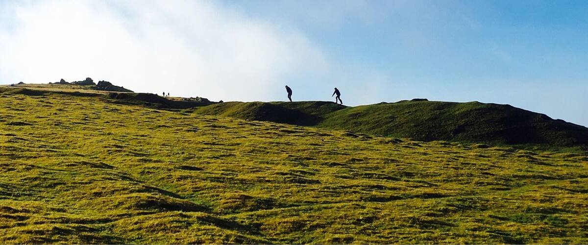 A grassy hill with two people walking.