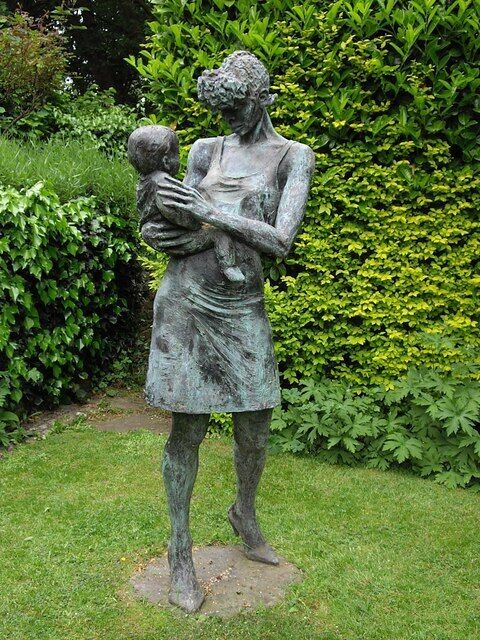 A bronze statue of a woman holding a child in a garden.
