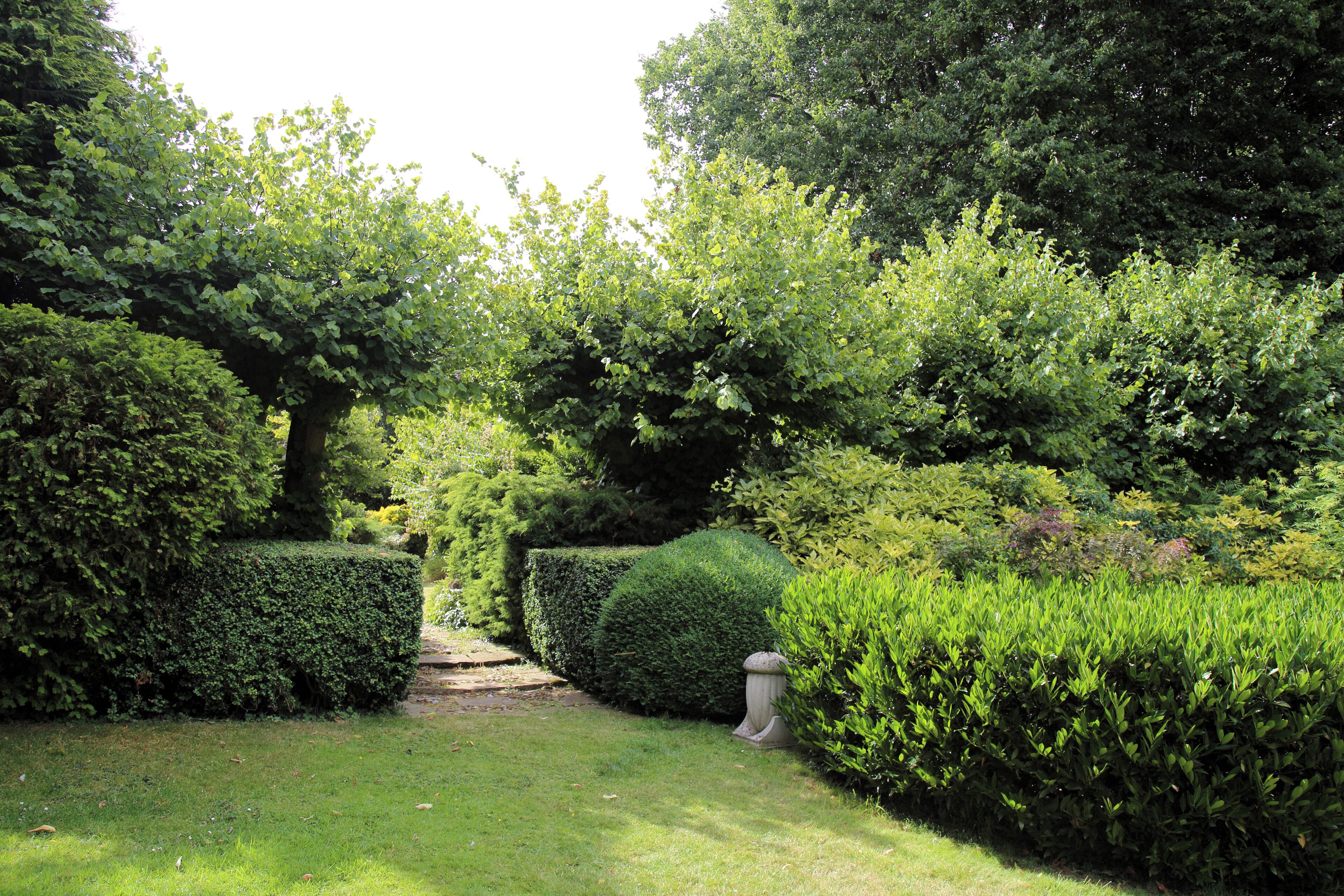 A well-maintained garden with neatly trimmed hedges, a variety of trees, and a stone pathway.