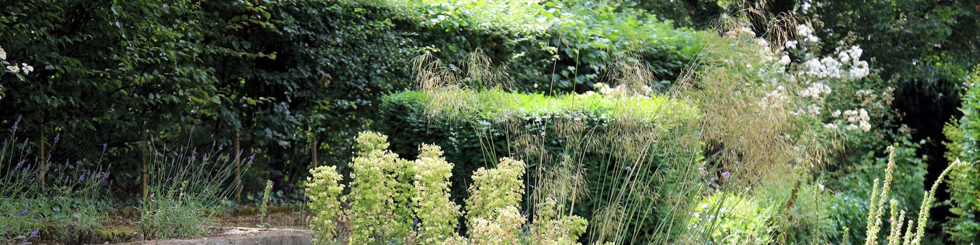 A hedge-backed lawn flower and shrub bed, and brick wall, at The Gibberd Garden, in the Harlow District of Essex, England