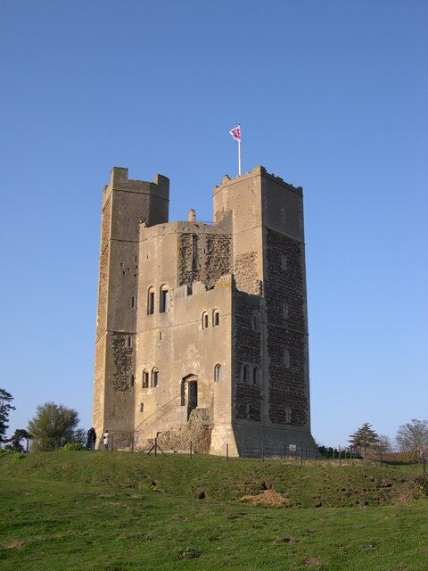 A medieval stone tower with a flag on top, surrounded by a grassy field.
