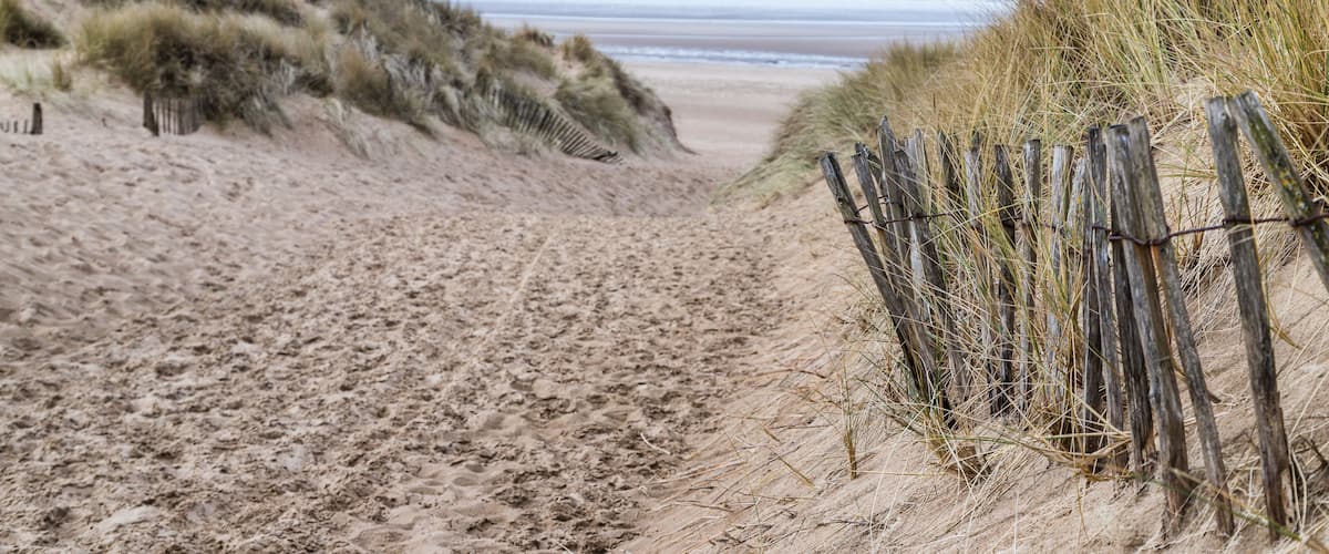 A sandy beach with dunes and a wooden fence.