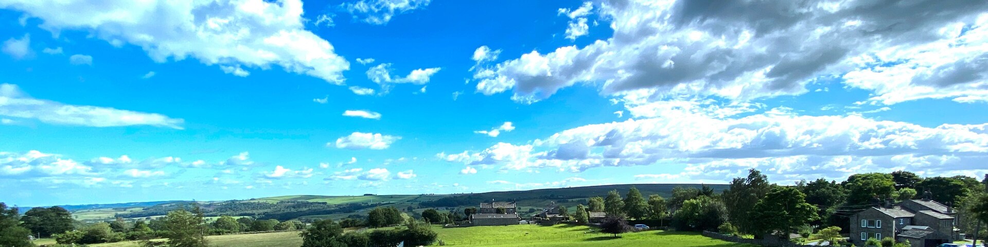 Un campo verde con ovejas, un pueblo y un cielo azul con nubes.