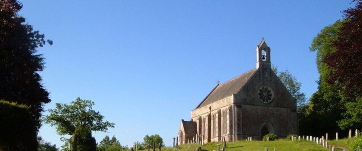 A church with a clock tower, surrounded by a cemetery and lush greenery.