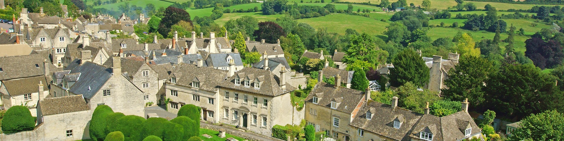 A historic village with stone buildings, a well-maintained garden, and rolling green hills in the background.