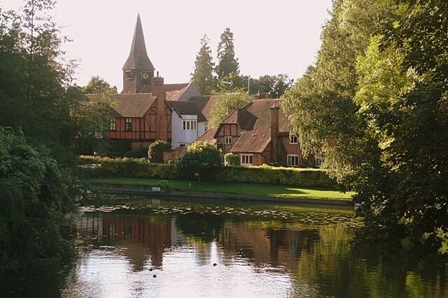 Whitchurch from the toll bridge St. Mary the Virgin church, Whitchurch, and its surrounding buildings around the mill stream on the north bank of the Thames.
