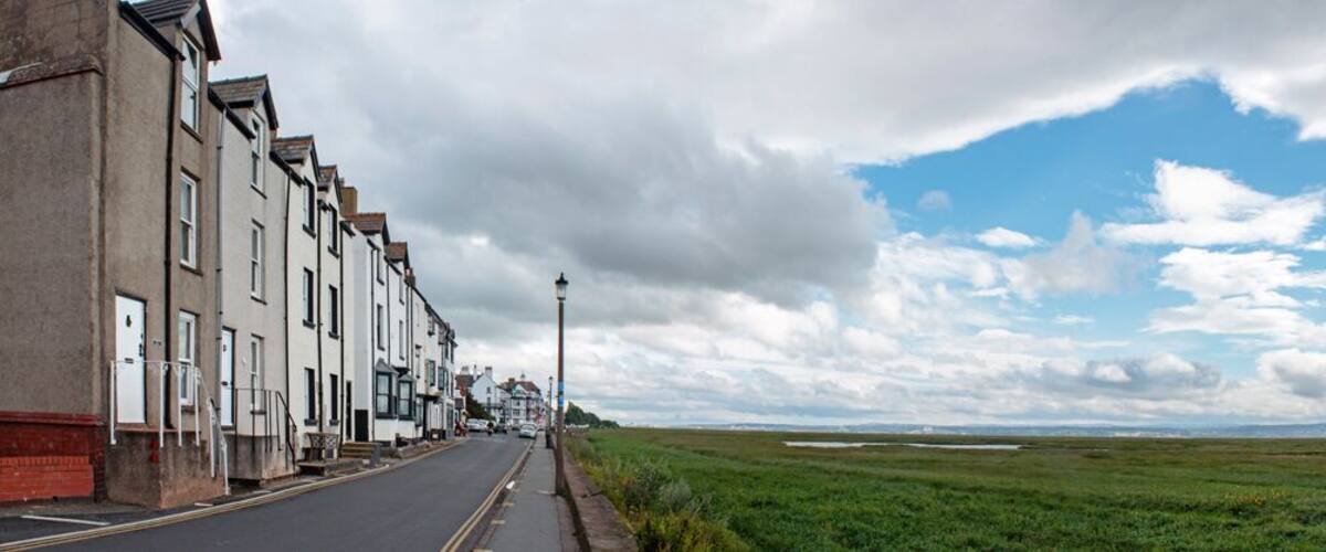 A street lined with terraced houses, a lamppost, and a flat landscape with distant hills under a partly cloudy sky.