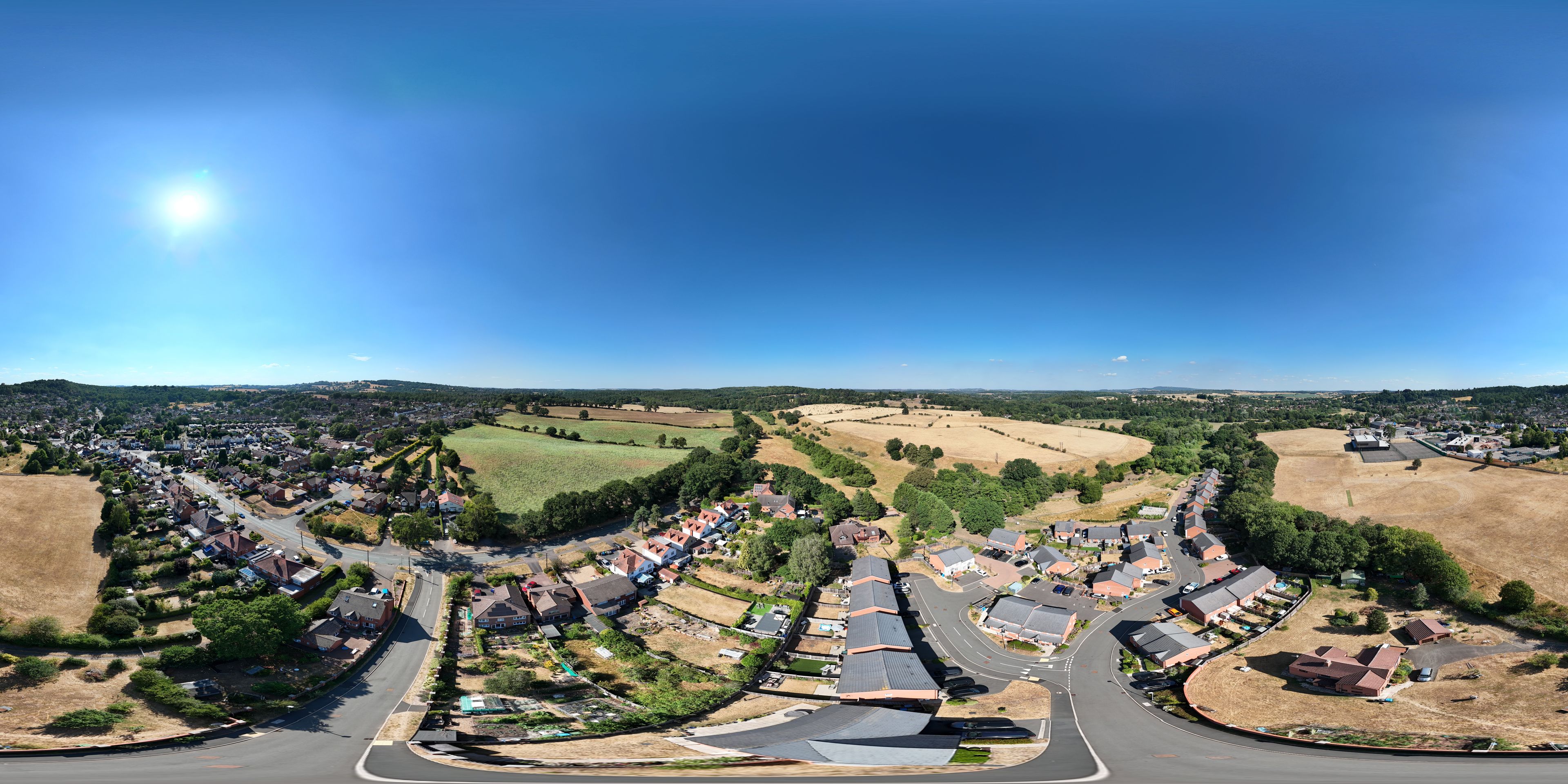 Una vista panorámica de un pueblo con casas residenciales, campos verdes y un cielo azul despejado.