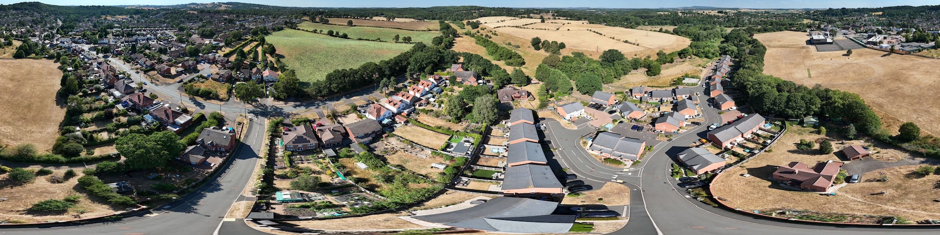 A panoramic view of a town with a mix of residential houses, green fields, and a clear blue sky.