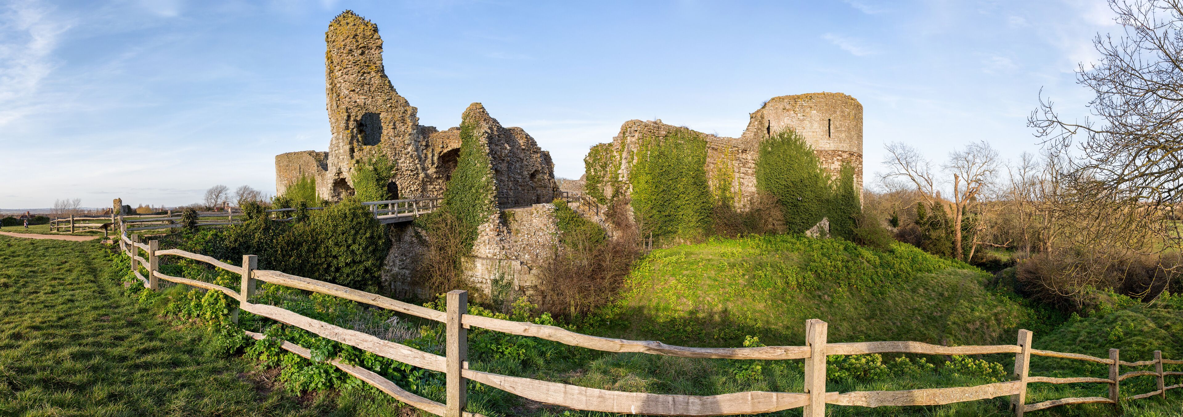 A historic stone castle ruin with ivy-covered walls and a wooden fence in the foreground.