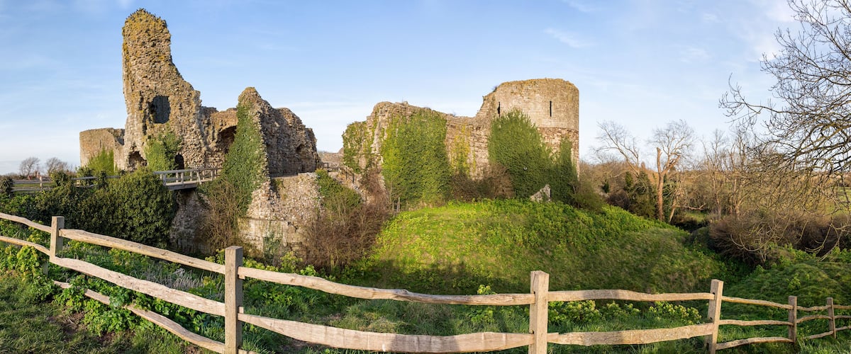 A historic stone castle ruin with ivy-covered walls and a wooden fence in the foreground.