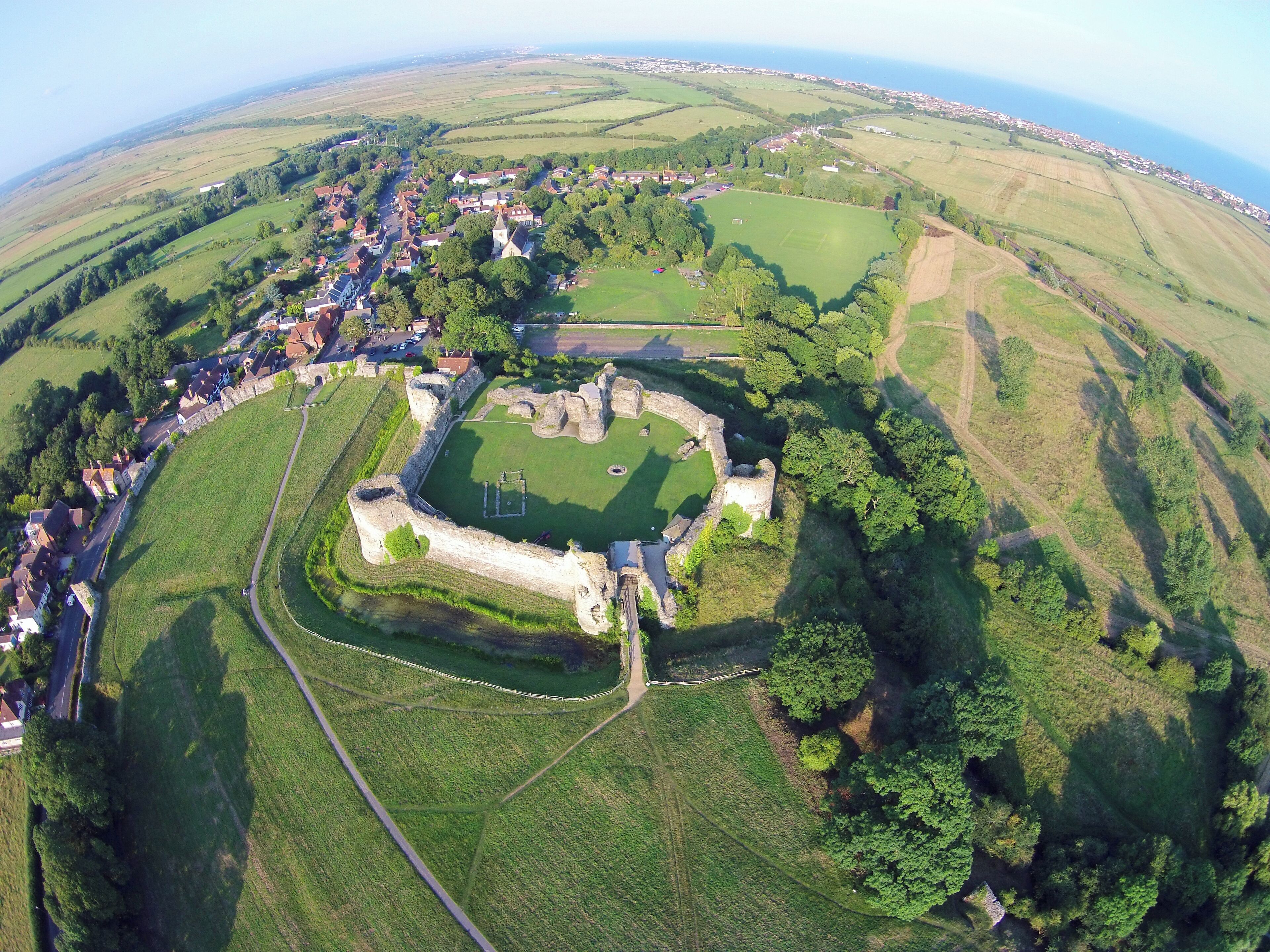 An aerial view of a historic fort surrounded by a village, with rolling hills and a coastal backdrop.