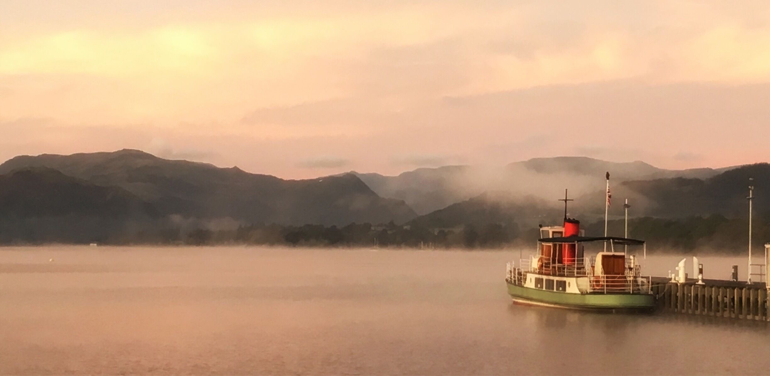 A boat docked at a pier with misty mountains in the background.