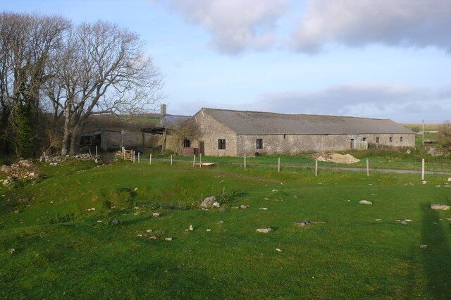 A rural barn with a stone roof, surrounded by a fenced pasture and leafless trees.