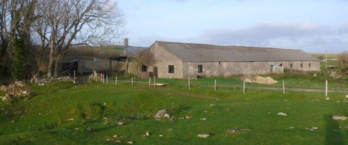 A rural barn with a stone roof, surrounded by a fenced pasture and leafless trees.