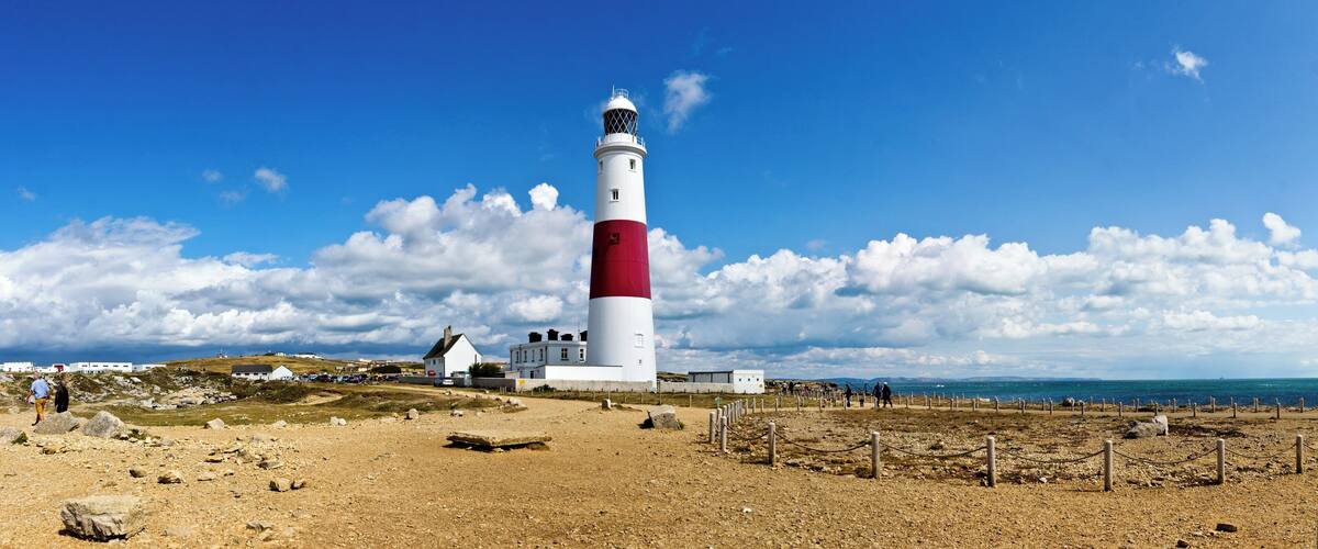 A white and red lighthouse with a clear blue sky and clouds in the background.