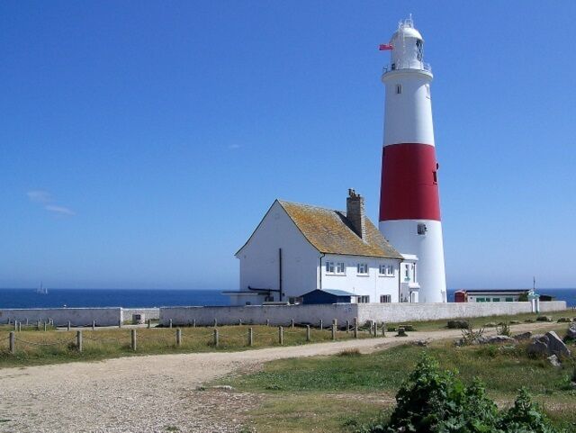 A lighthouse with a red and white striped tower next to a white building with a red roof.