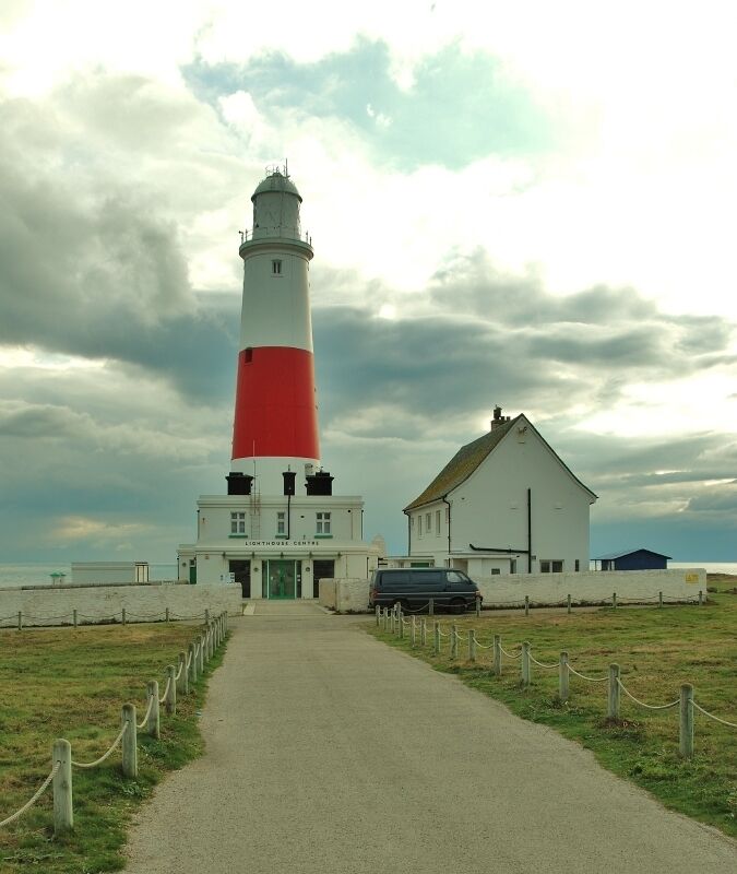 A lighthouse with a red and white tower, a white building with a green door, and a car parked in front.