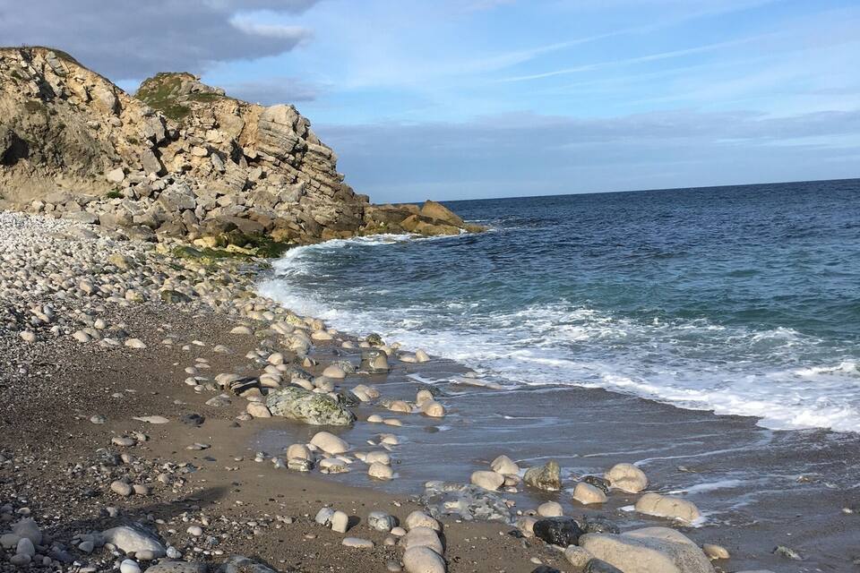 Platja rocosa amb onades que es trenquen a la riba i un penya-segat al fons.