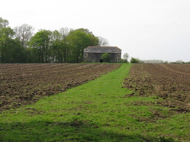A rural landscape with a plowed field, a grassy path, and a stone building in the distance.